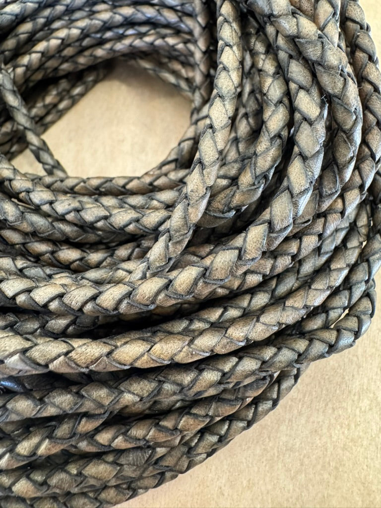 A grey, machine-braided leather bolo cord with plastic tips.
