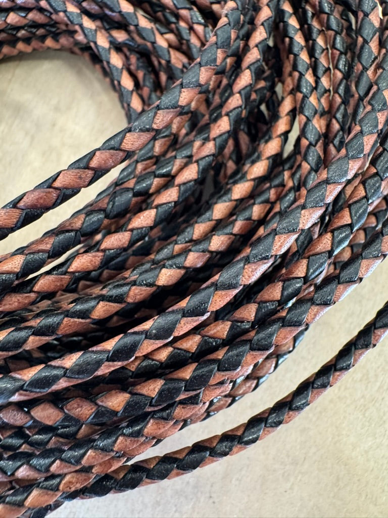 A black and brown, machine-braided leather bolo cord with plastic tips.